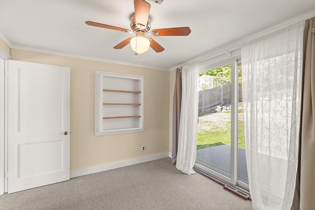 carpeted empty room with baseboards, ornamental molding, ceiling fan, visible vents, and built in shelves