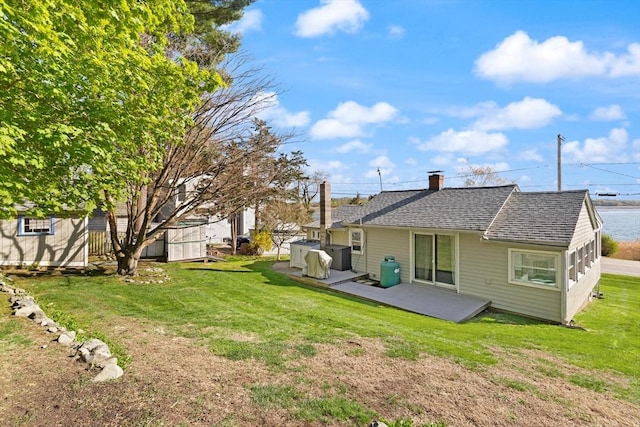 back of property featuring an outbuilding, a storage unit, a chimney, a shingled roof, and a yard