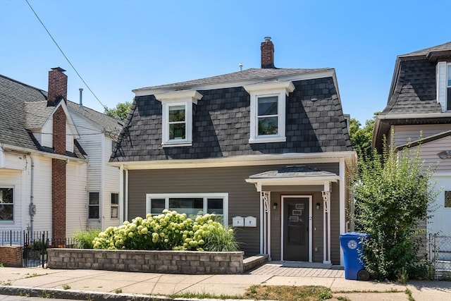 view of front of property featuring fence, mansard roof, and roof with shingles