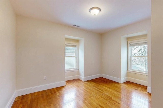 unfurnished room featuring visible vents, light wood-type flooring, and a wealth of natural light