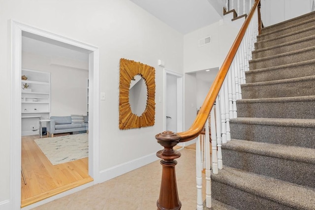 stairs featuring visible vents, baseboards, a high ceiling, tile patterned floors, and built in shelves