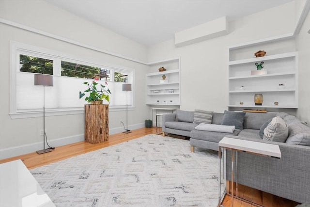 living area with built in features, baseboards, and light wood finished floors