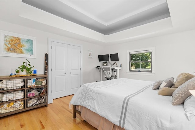 bedroom featuring a closet, a raised ceiling, and light wood finished floors
