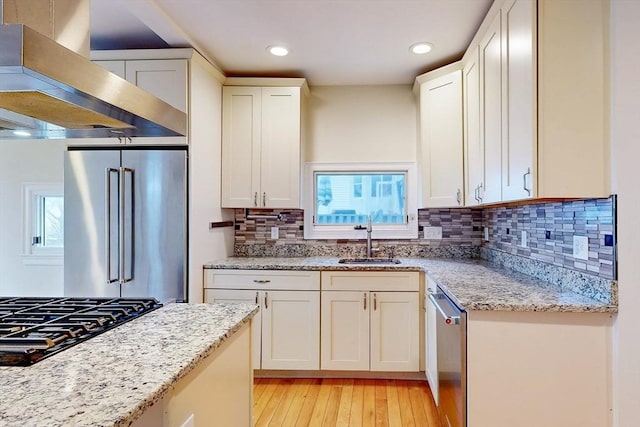 kitchen featuring exhaust hood, appliances with stainless steel finishes, a sink, white cabinetry, and light wood-type flooring