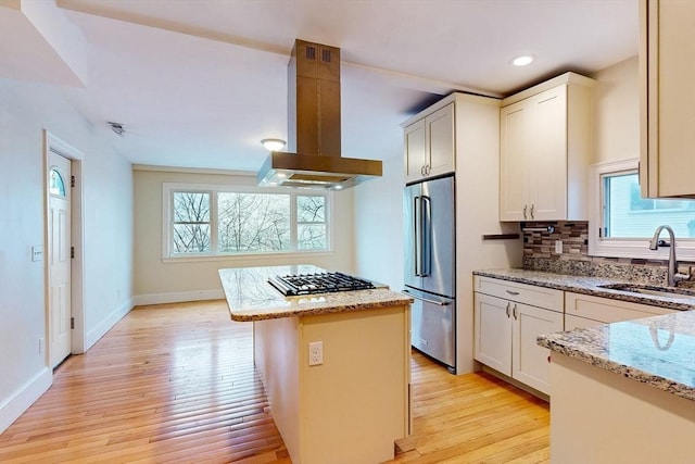 kitchen featuring high end fridge, gas cooktop, a sink, island exhaust hood, and a kitchen island