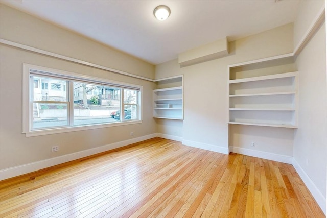 spare room with light wood-style floors, baseboards, and built in shelves