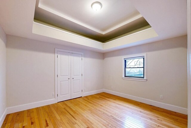 empty room featuring baseboards, light wood finished floors, and a tray ceiling
