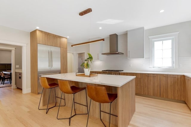 11 Cuba St, Andover, MA 01810 - kitchen with a breakfast bar area, a center island, light wood finished floors, modern cabinets, and wall chimney range hood