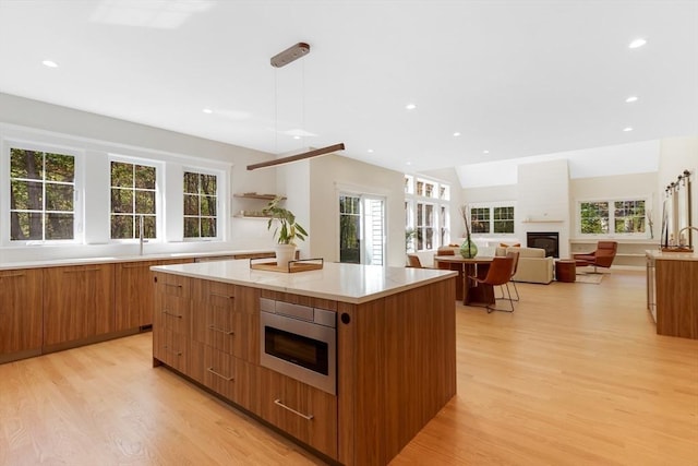 11 Cuba St, Andover, MA 01810 - kitchen with brown cabinetry, modern cabinets, a glass covered fireplace, a kitchen island, and light wood-type flooring