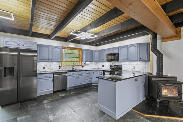 kitchen featuring black appliances, dark countertops, a peninsula, gray cabinets, and a wood stove