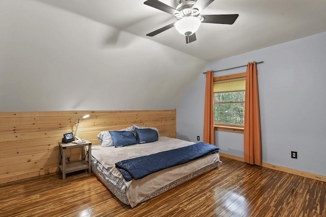 bedroom featuring wood finished floors, lofted ceiling, wood walls, baseboards, and a ceiling fan