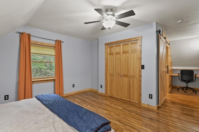 bedroom with wood finished floors, a barn door, baseboards, ceiling fan, and lofted ceiling