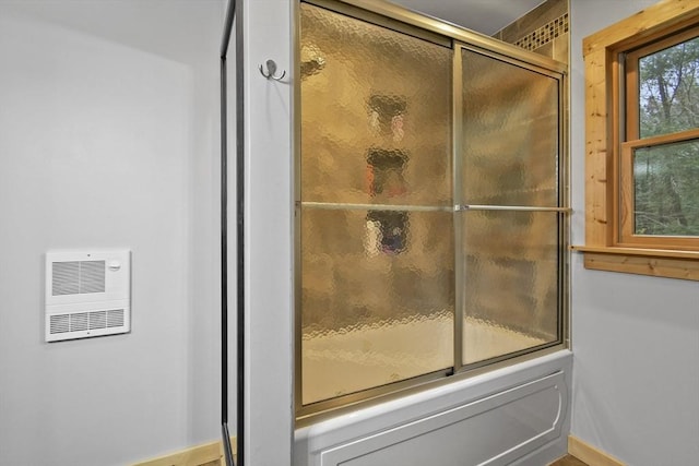 bathroom featuring heating unit, shower / bath combination with glass door, and baseboards