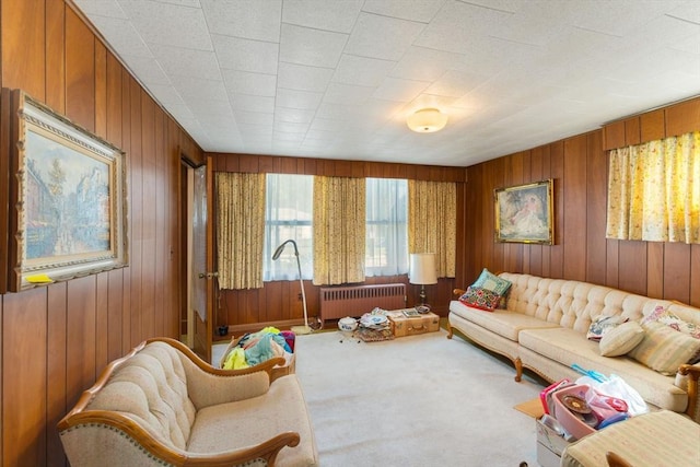 living area with radiator heating unit, carpet, and wood walls