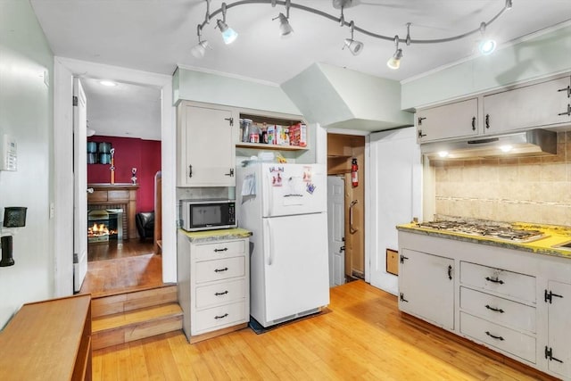 kitchen with white cabinetry, a brick fireplace, appliances with stainless steel finishes, tasteful backsplash, and light hardwood / wood-style flooring