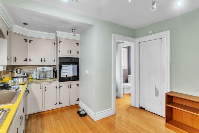 kitchen featuring backsplash, sink, light hardwood / wood-style flooring, white cabinets, and black oven