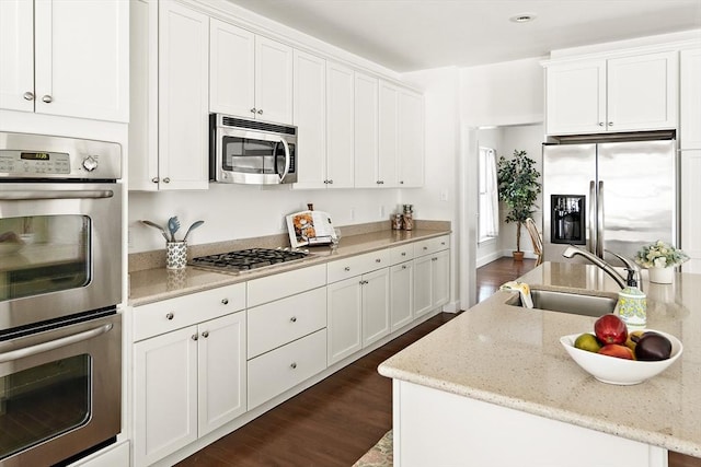 kitchen featuring light stone countertops, white cabinetry, a kitchen island with sink, sink, and stainless steel appliances