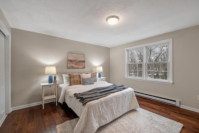 bedroom featuring baseboard heating, a textured ceiling, baseboards, and wood finished floors