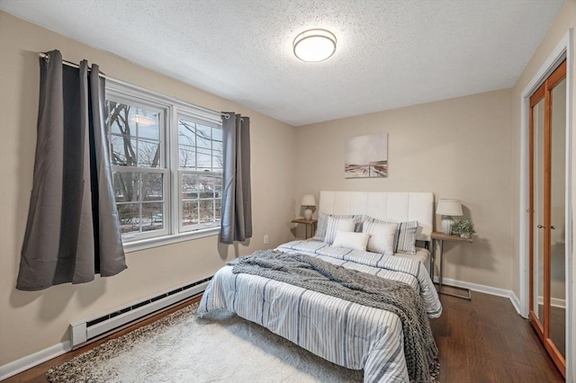 bedroom with a baseboard heating unit, wood finished floors, baseboards, and a textured ceiling