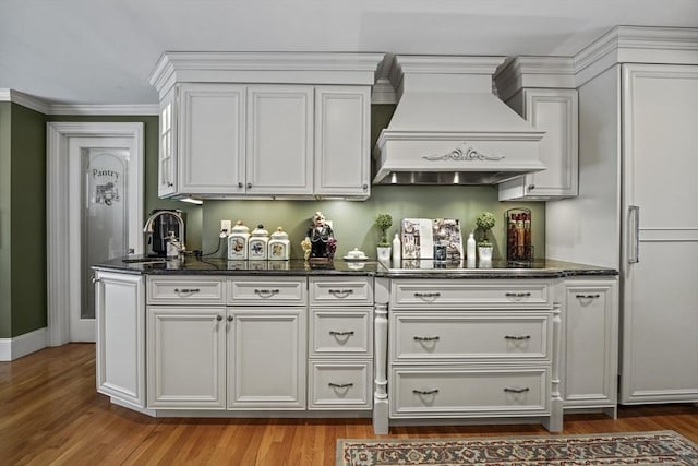 kitchen featuring wood finished floors, premium range hood, a sink, and white cabinets