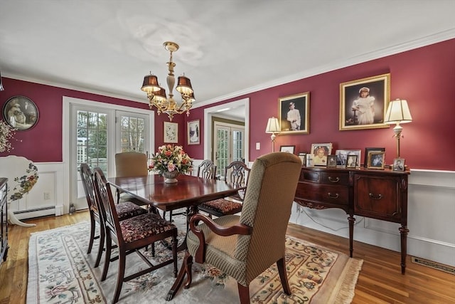 dining area featuring a wainscoted wall, ornamental molding, wood finished floors, baseboard heating, and a notable chandelier