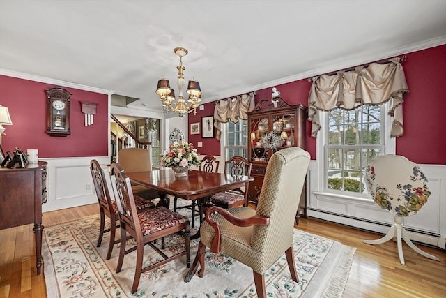 dining area with a wainscoted wall, a baseboard radiator, light wood-style flooring, ornamental molding, and a chandelier