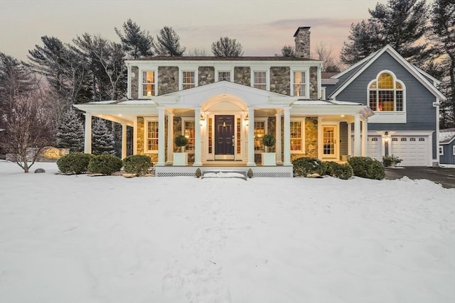 view of front of property featuring a garage, stone siding, a chimney, aphalt driveway, and covered porch