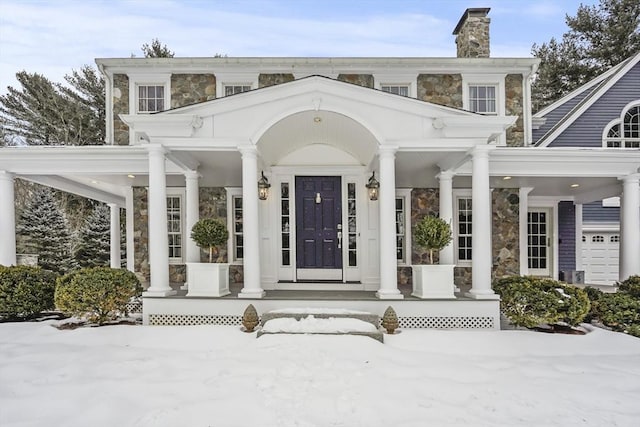 snow covered property entrance with stone siding, covered porch, and a chimney