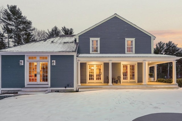 snow covered back of property featuring covered porch and french doors