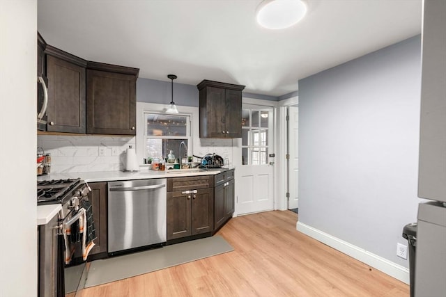 kitchen featuring dark brown cabinetry, stainless steel appliances, light countertops, light wood finished floors, and decorative light fixtures