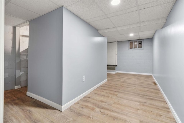 interior space with light wood-type flooring, baseboards, a paneled ceiling, and concrete block wall