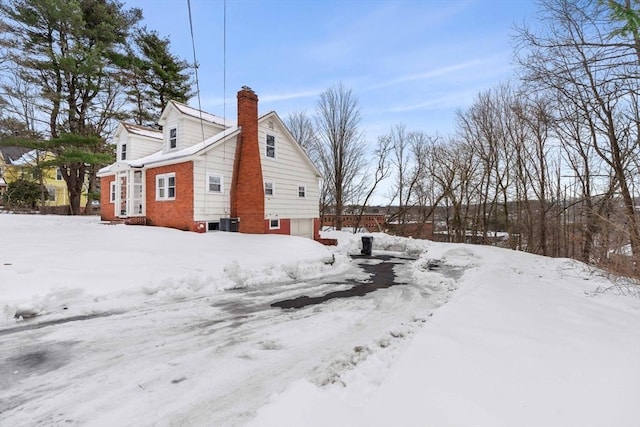 snow covered property with a chimney and an attached garage