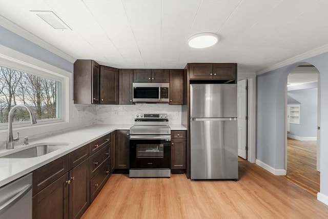 kitchen with arched walkways, a sink, light countertops, appliances with stainless steel finishes, and tasteful backsplash