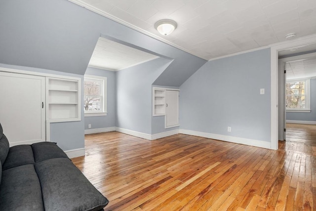 bonus room with vaulted ceiling, built in shelves, light wood-type flooring, and baseboards