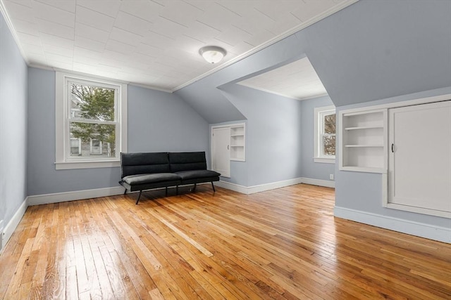 living area with ornamental molding, lofted ceiling, light wood-style flooring, and baseboards