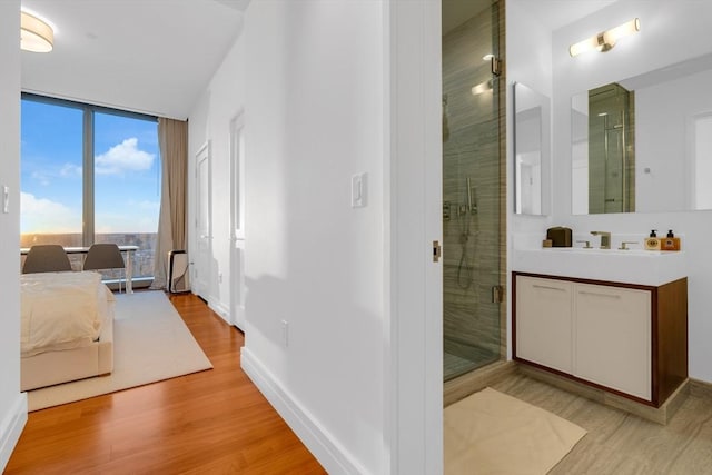 bathroom featuring floor to ceiling windows, vanity, a shower stall, wood finished floors, and baseboards