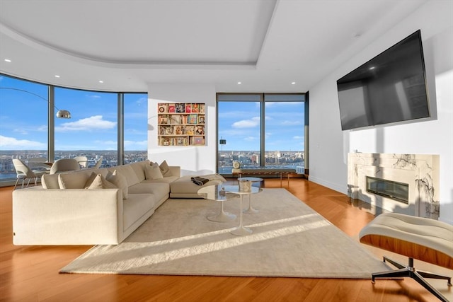 living area featuring expansive windows, a premium fireplace, a tray ceiling, and wood finished floors