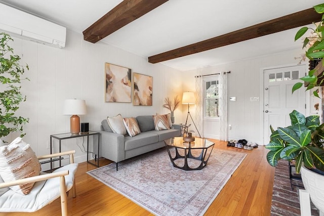 living room featuring beam ceiling, wood finished floors, and a wall mounted AC