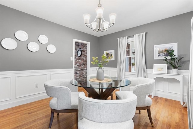 dining area with a decorative wall, a wainscoted wall, a chandelier, and light wood-type flooring
