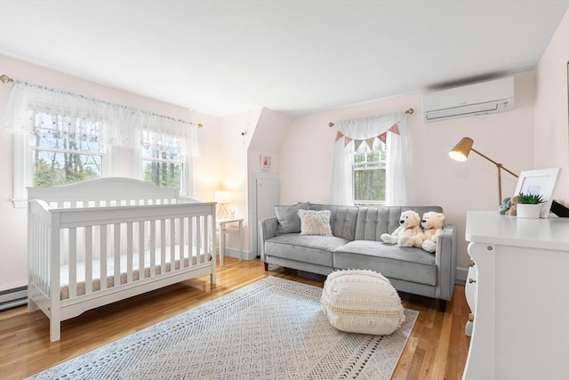 bedroom with a wall mounted air conditioner, a crib, and light wood-style flooring