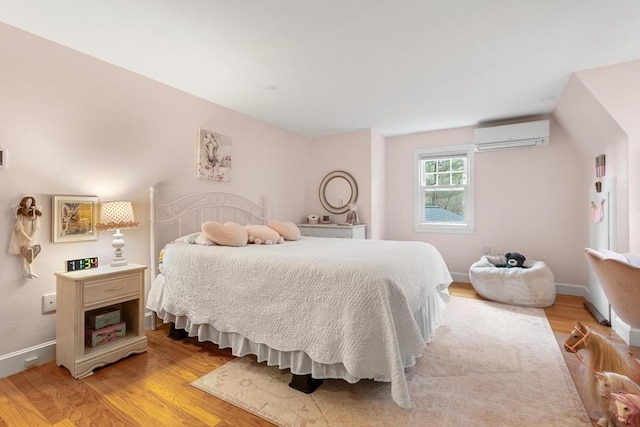 bedroom with baseboards, light wood finished floors, and a wall mounted AC