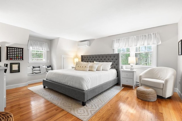 bedroom featuring baseboards, a baseboard heating unit, light wood finished floors, and a wall mounted AC