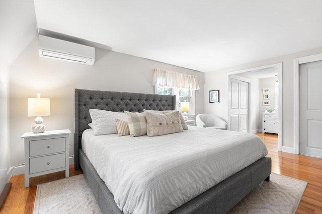 bedroom with baseboards, a wall mounted AC, and light wood-type flooring
