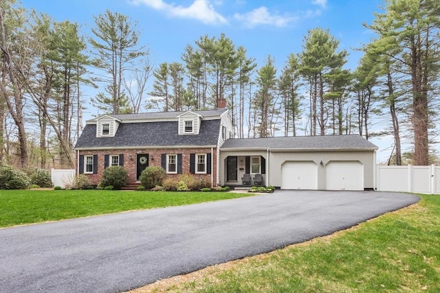 colonial inspired home with aphalt driveway, a chimney, an attached garage, fence, and brick siding