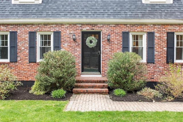 view of exterior entry featuring roof with shingles and brick siding
