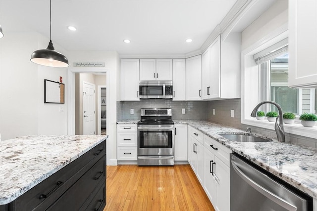 kitchen with white cabinetry, decorative backsplash, a sink, appliances with stainless steel finishes, and decorative light fixtures