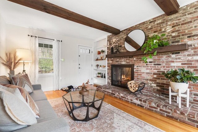 living room featuring wood finished floors, built in shelves, beamed ceiling, and a brick fireplace