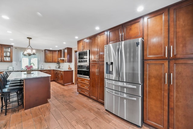 kitchen with light stone countertops, a center island, appliances with stainless steel finishes, a kitchen bar, and decorative light fixtures