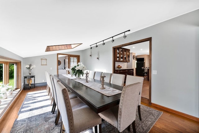 dining area featuring vaulted ceiling with skylight and light hardwood / wood-style flooring