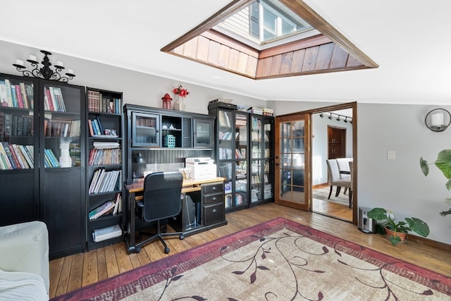 office with wood-type flooring, vaulted ceiling with skylight, and french doors